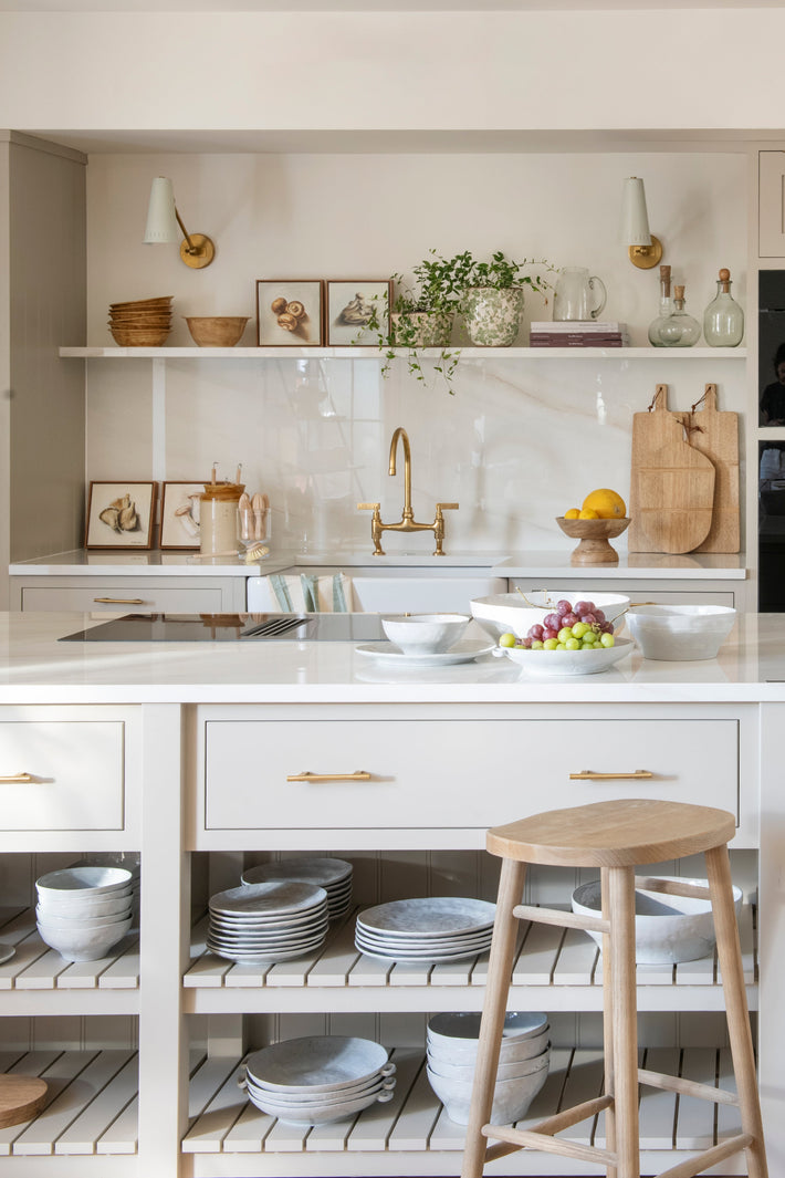 Close-up of the kitchen island with open shelving, displaying ceramics and glassware, with the polished brass bridge mixer visible in the background.