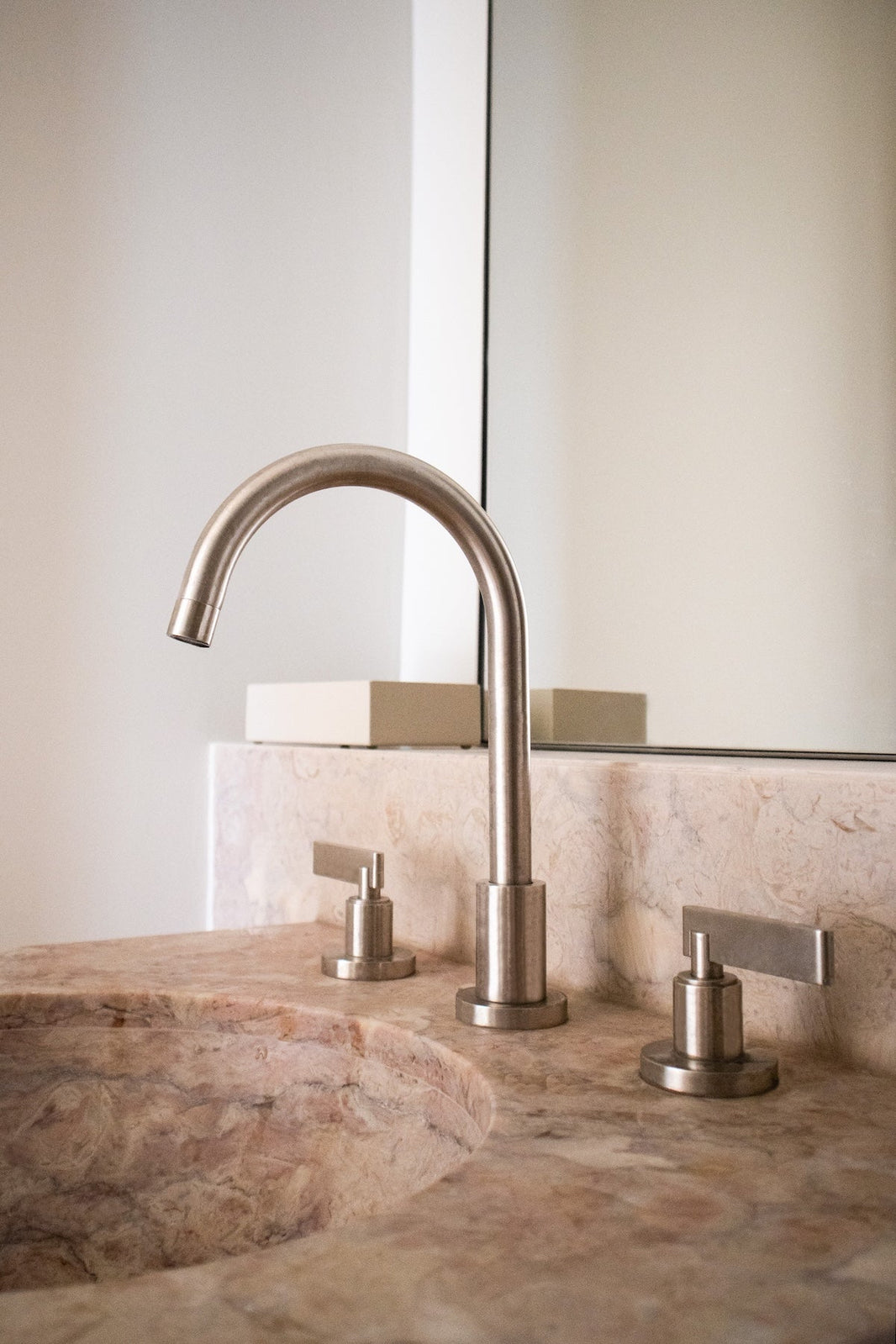 From Chapter One, a three hole deck mounted basin tap in brushed nickel stands over a blush pink marble sink.