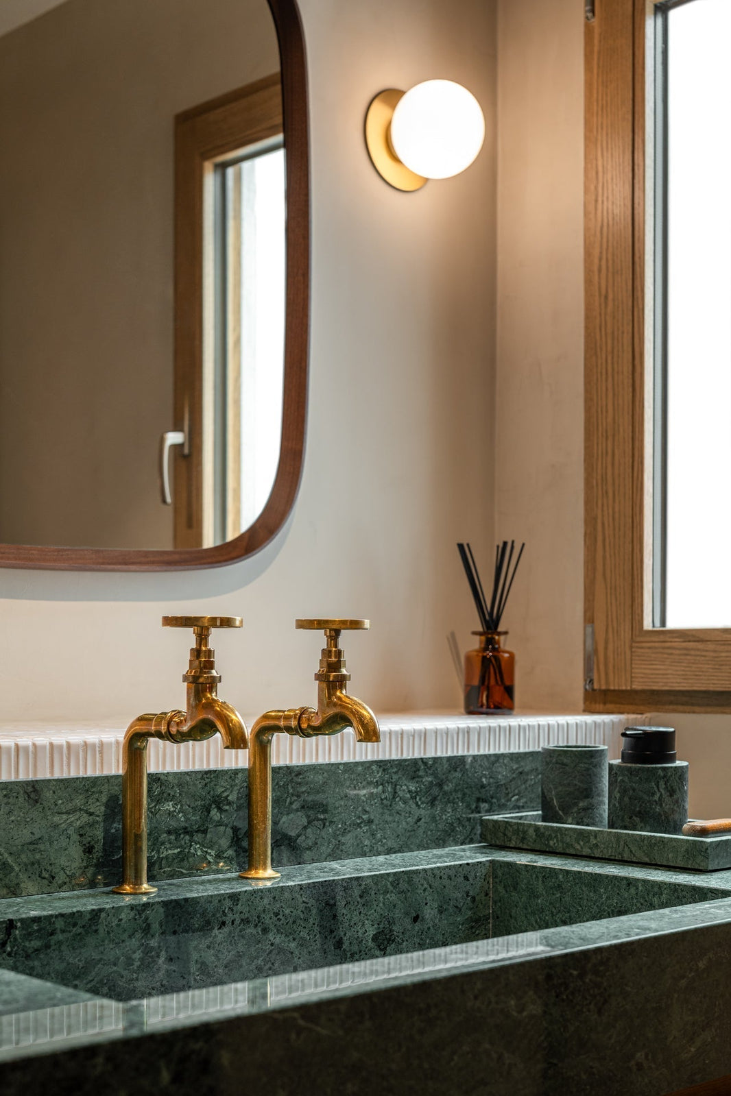 Studio Ore's solid brass bib taps are found in this apartment renovation in Barcelona. Here, unlacquered polished brass bib taps stand over a long, deep green marble sink. 