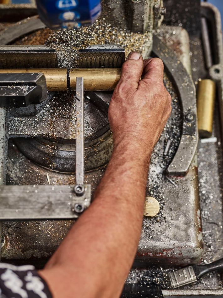 A solid brass bar being cut in Studio Ore's workshop. It's a tough process. The machines are big. There's metal dust everywhere. 