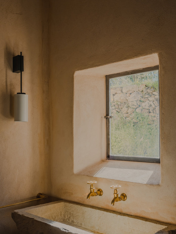 Studio Ore fittings are found in this project by Ibiza Interiors. The polished brass bib taps are wall mounted, over a large, rectangular stone basin. 