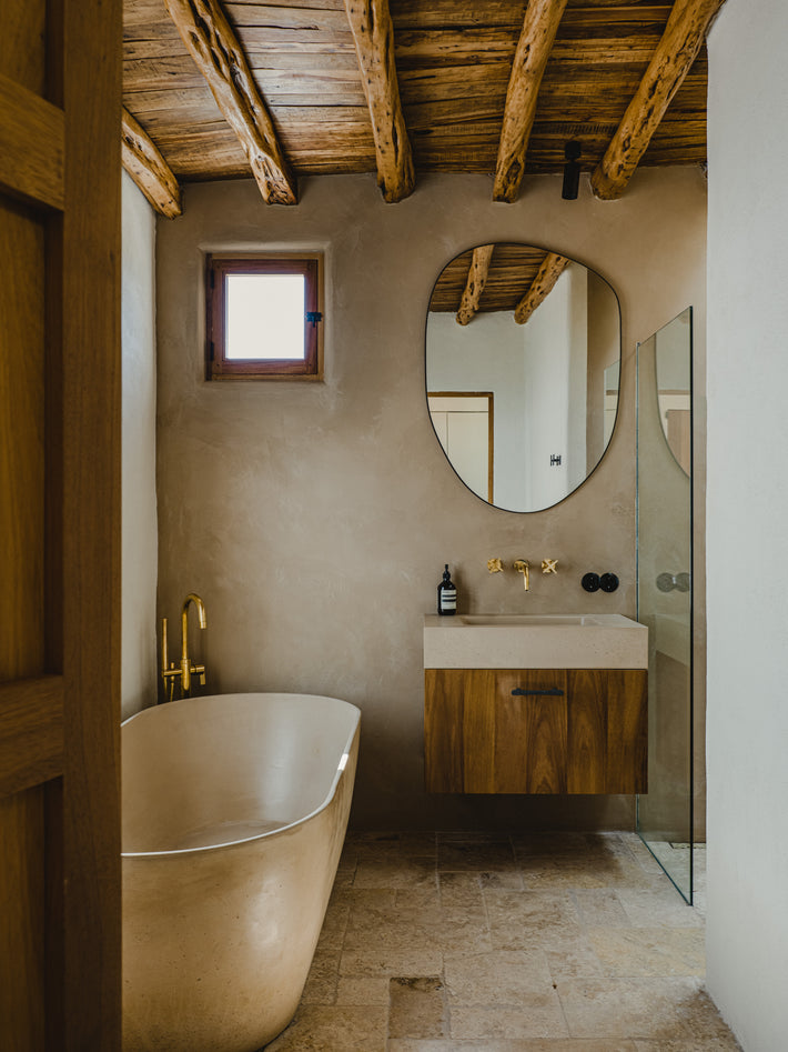 Bathroom interior at Ibiza Campo Casa featuring Studio Ore wall mounted taps and exposed shower in Unlacquered Brass, paired with natural stone and timber ceiling beams.