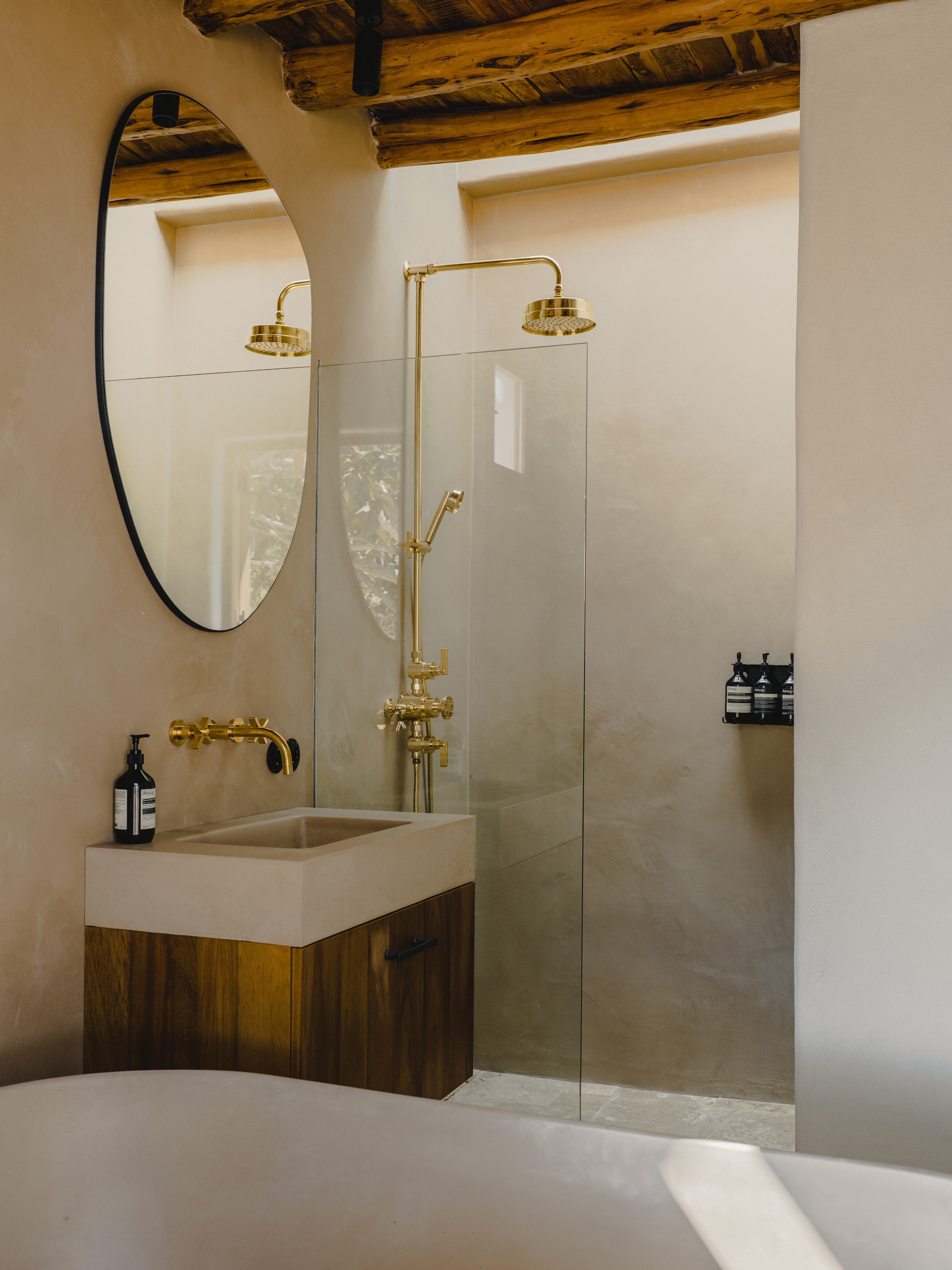 Studio Ore triple exposed shower thermostat with overhead shower in Unlacquered Brass at Ibiza Campo Casa, set against lime plaster walls with timber ceiling beams.