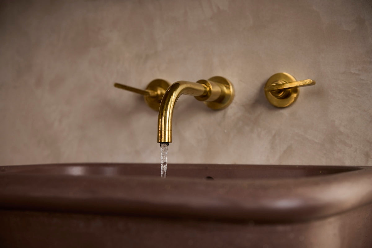 A close-up of Studio Ore's wall mounted basin tap from Chapter One in unlacquered polished brass. 