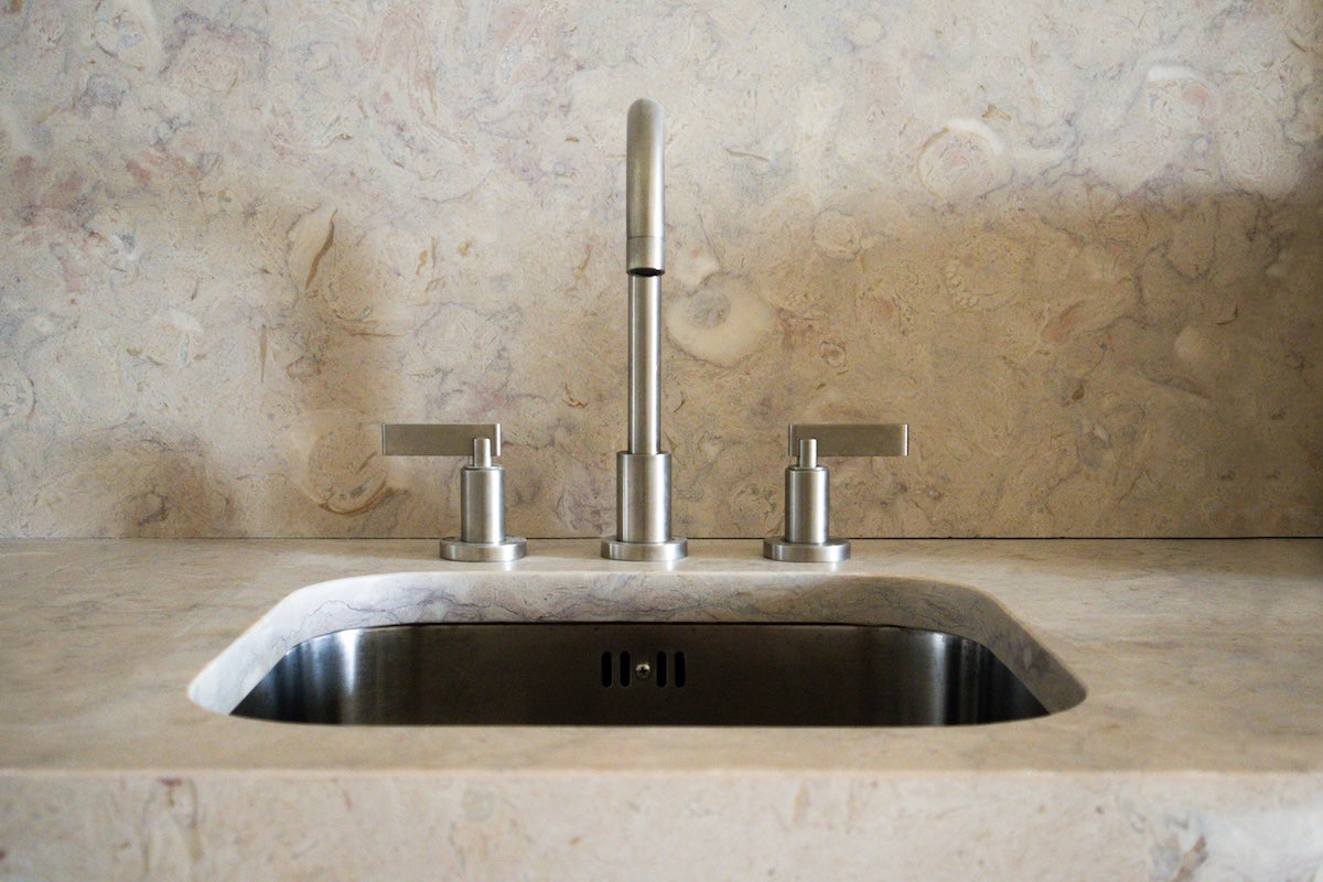 Studio Ore fittings can be found in Lioz, a hotel in Lisbon designed by REABILITA. The design is minimal. Here, the three hole deck mounted basin tap is in the kitchen, standing over the sink. Neutral toned marble covers the surfaces and back splash.