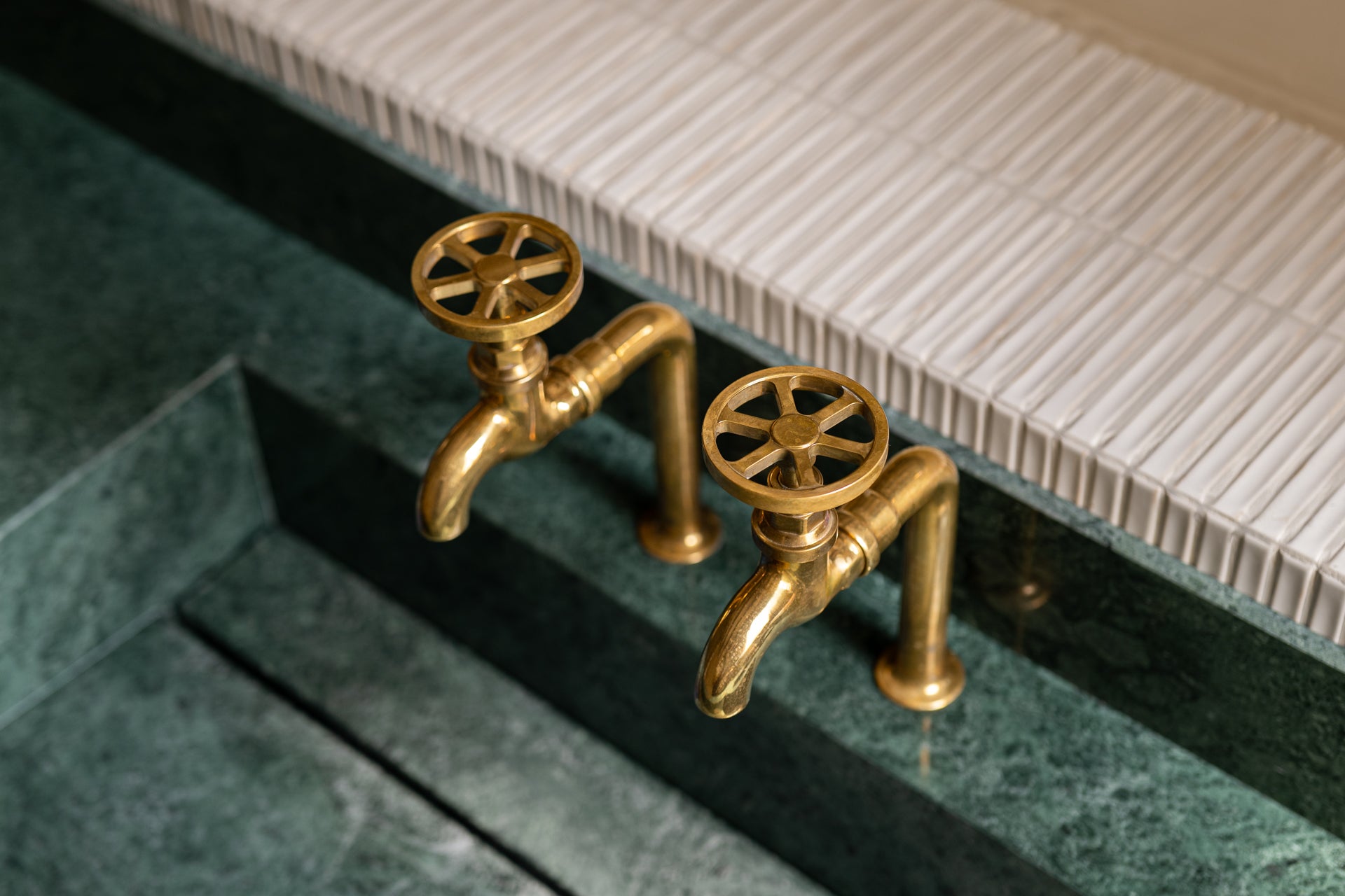 Studio Ore's solid brass bib taps are found in this apartment renovation in Barcelona. Here, unlacquered polished brass bib taps stand over a long, deep green marble sink. 