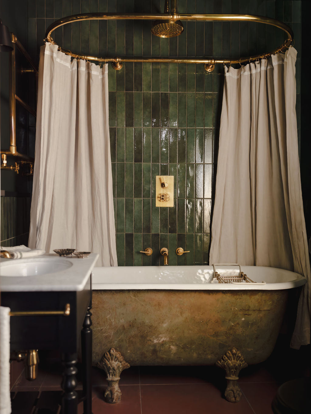 Bathroom with freestanding clawfoot tub and brass fittings, green tiled wall, and brass shower system with curtain rail.