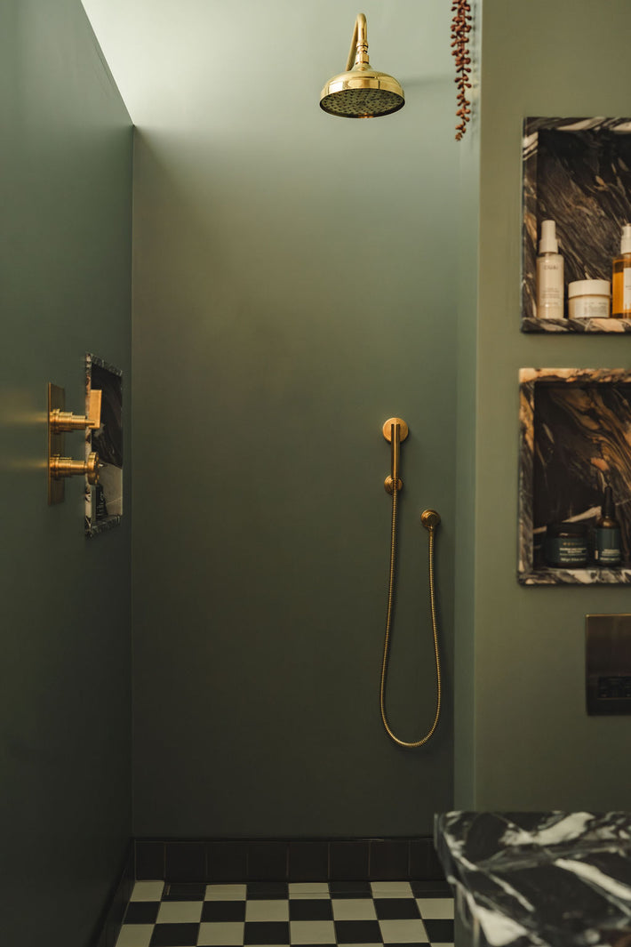 Minimalist shower wall with brass handheld shower and hose.