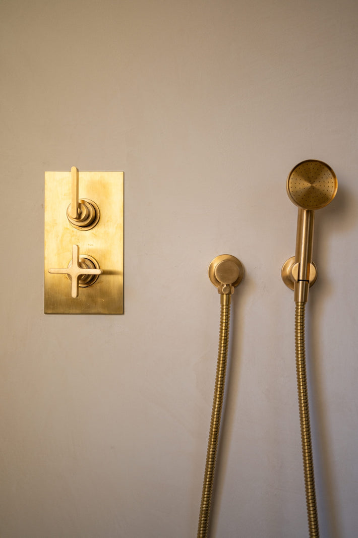 Studio Ore fittings can be found in this bathroom designed by Tristan Domecq. Here, the polished brass shower thermostat and hand shower are wall-mounted. The wall colour has a lime wash look. 