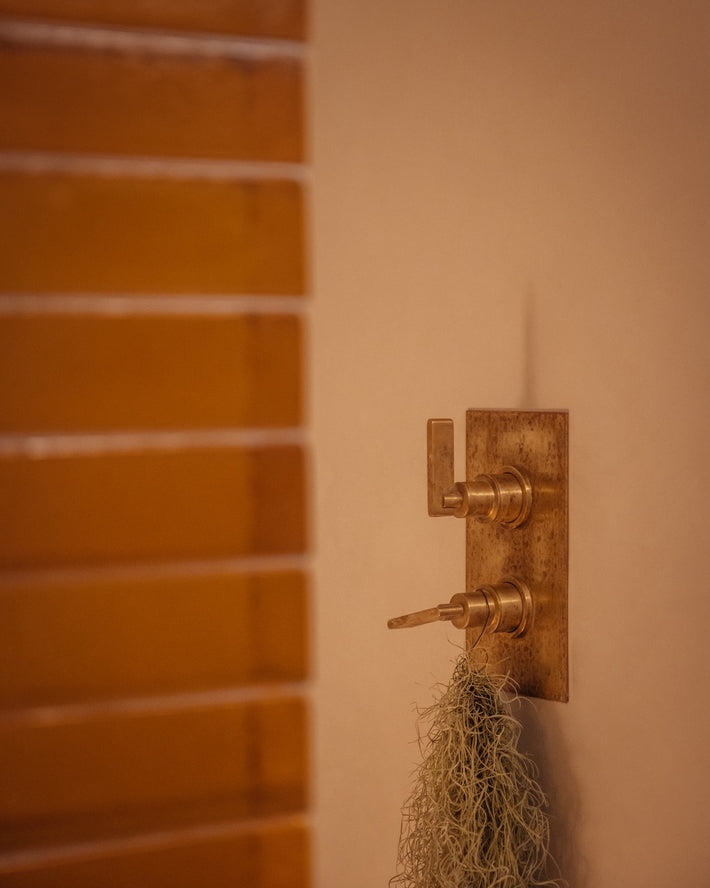 Studio Ore's dual shower thermostat in polished brass, wall mounted in a modern bathroom.